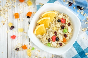 Homemade oatmeal porridge with honey, orange, raisin, peanut and candied fruit on white wooden background. Healthy breakfast.