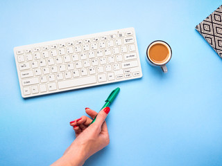 Keyboard, woman's hand with a pen, cup of coffee. Writing, studying and blogging concept. Blue pastel minimal background