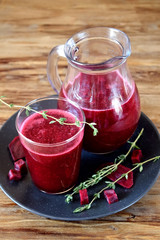 Beet smoothie in a glass and a jug. Thyme and beetroot pieces are around
