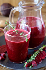 Beet smoothie in a glass and a jug. Thyme and beetroot pieces are around