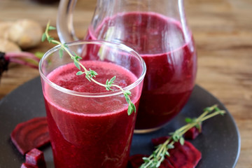 Beet smoothie in a glass and a jug. Thyme and beetroot pieces are around