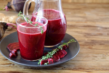 Beet smoothie in a glass and a jug. Thyme and beetroot pieces are around
