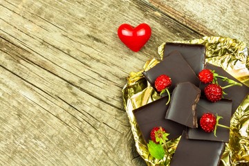 Bitter chocolate in a gold foil on a wooden board. Chocolate delicacy. Wild strawberries.