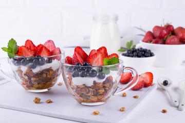 Homemade Greek yogurt with granola, mint, blueberries and strawberry in a glass cups on white...
