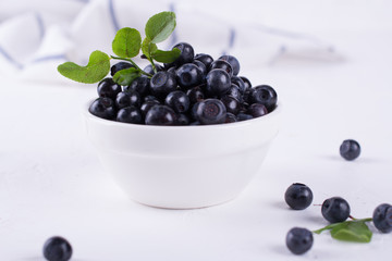 Fresh blueberries with green leaf  in a white bowl on a white background