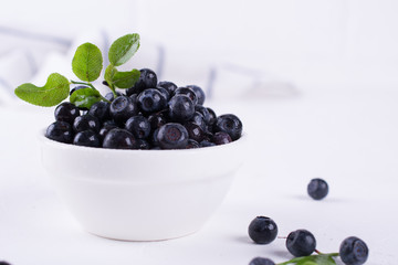 Fresh blueberries with green leaf  in a white bowl on a white background