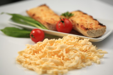 Shredded cheese next to a plate with two cheese sandwiches