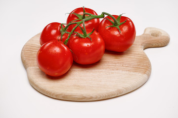 Several tomatoes lie on a wooden cutting board.
