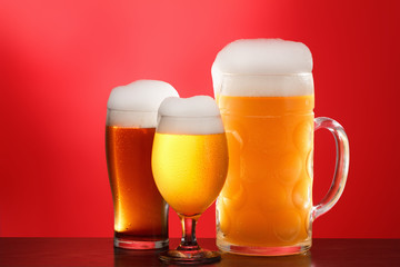 Mug and glass of beer close-up with froth over red background
