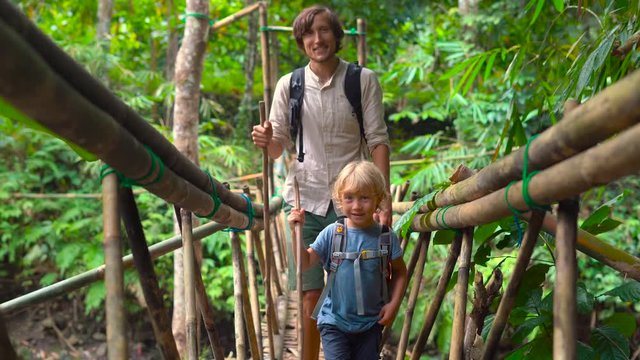 Father an som crossing tropical river on a bridge made of a bamboo