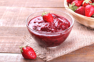 Strawberry jam in a glass bowl and with fresh strawberries on a brown wooden background