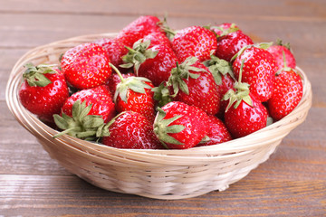 A lot of ripe strawberries in a wicker basket on a brown wooden background