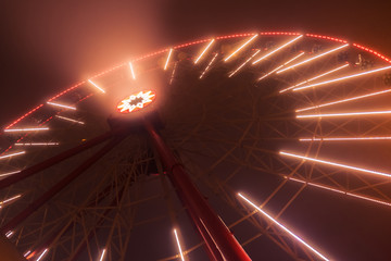 Luminous ferris wheel at night in a fog, high carousel