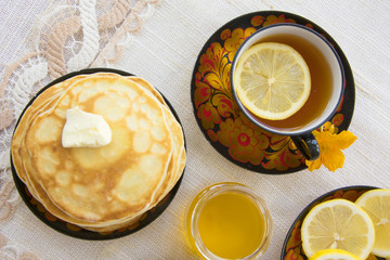 tea in a painted Cup, on a saucer sliced lemon, pancakes, sour cream and a wooden spoon for overlaying. tea party in rustic style