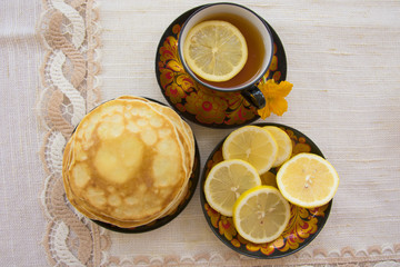 tea in a painted Cup, on a saucer sliced lemon, pancakes, sour cream and a wooden spoon for overlaying. tea party in rustic style