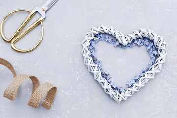 Close-up photo of cute heart shape with blue little flowers on gray table background with golden scissors . Top view