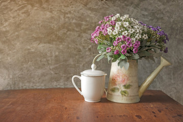 Obraz na płótnie Canvas Flower bouquet in white water can and white coffee cup place on wood desk with Polished cement wall.Retro design image.