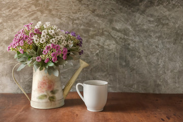 Flower bouquet in white water can and white coffee cup place on wood desk with Polished cement wall.Retro design image.