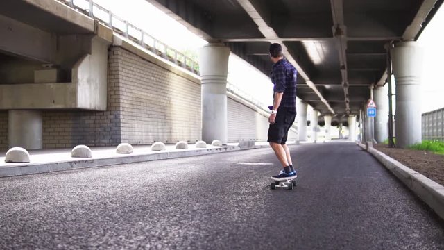 A man riding a skateboard on the asphalt on the background of the overpass