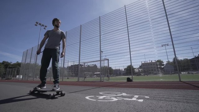 Electric Longboard summer ride on red sport stadium with playground