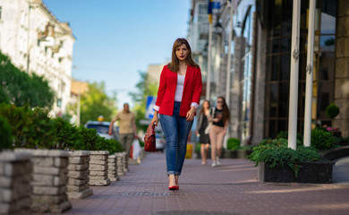 a girl in a red jacket and a lady's bag is walking along the street