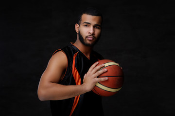 Naklejka premium Young African-American basketball player in sportswear isolated over dark background.