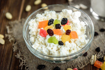 Cottage cheese with candied fruit, raisins, peanuts and glass of milk or kefir on dark wooden background. Healthy food for breakfast, snack or dinner.
