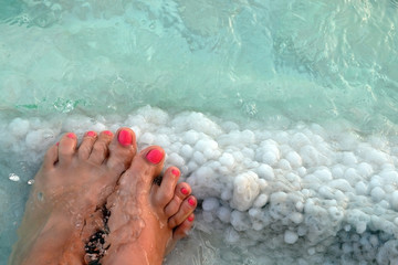Female feet with manicure on stone, covered with salt formations between the waves in the water....