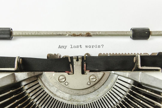 The text Any last words?, on a white paper page in an old vintage typewriter. Macro detail shot.
