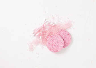 Scattered pink salt with pink sponges and cotton buds on white.