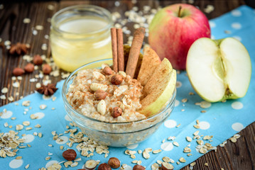 Homemade oatmeal with apple, cinnamon, hazelnuts, honey and peanuts on dark wooden background. Healthy breakfast.