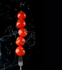 close up view of levitating cherry tomatoes on fork isolated on black