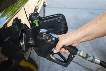 Man's hand holding nozzle of gas pump and putting gas into black car