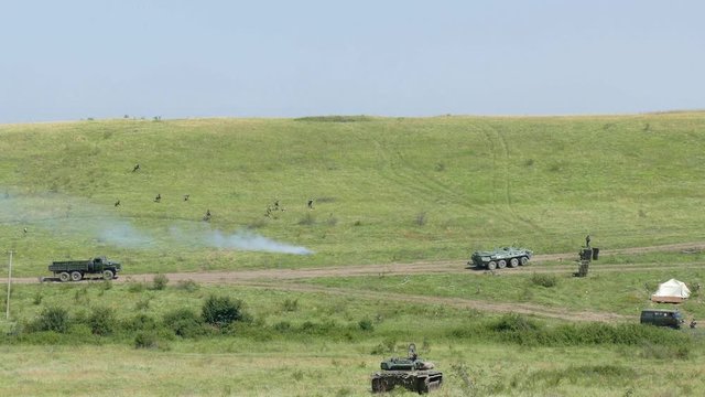 group of soldiers is moving along the slope of the mountain. on the perimeter is the military equipment. Soldiers make their way into the thought of a smoke bomb.