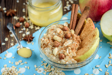 Homemade oatmeal with apple, cinnamon, hazelnuts, honey and peanuts on dark wooden background. Healthy breakfast.