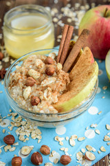 Homemade oatmeal with apple, cinnamon, hazelnuts, honey and peanuts on dark wooden background. Healthy breakfast.