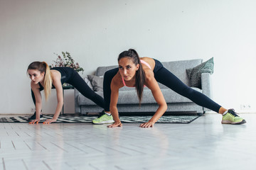 Fototapeta na wymiar Two fit girls doing home workout performing lateral lunges at home.