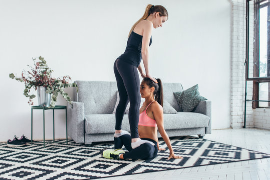 Woman helping friend in leg stretching workout at home