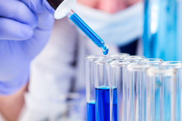 Scientist with pipette and test tubes and blue liquid water drop fall.