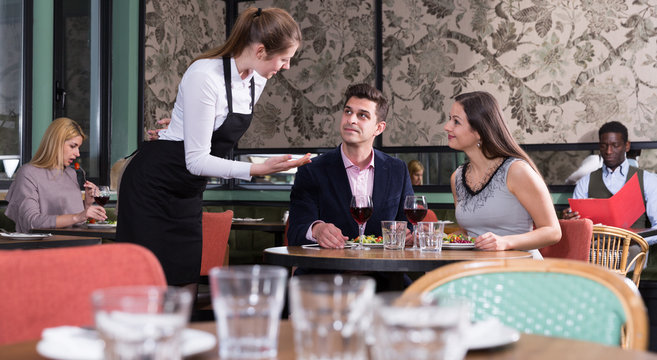 Waitress talking with satisfied couple in restaurant