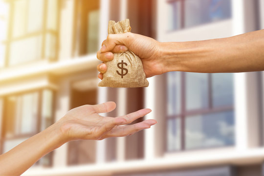 A man hand holding a money giving to another person for buying real estate. Loans for real estate concept. Conceptual give money to someone else to exchange real estate.