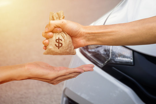 A man hand holding a money giving to another person for buying new car. Loans for new car concept. Conceptual give money to someone else to exchange new car.