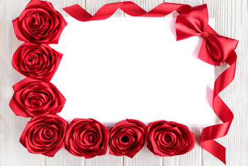 Blank white greeting card with red roses flowers and red ribbon bow on rustic wooden background. Top view. Valentines day or women's day.