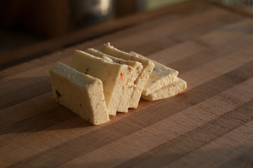 Sliced Cheese with pieces of paprika on wooden bamboo cutting board at home kitchen in morning