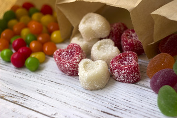 Sweets in paper bags. Multicolored candy, marmalade in the form of heart on a white wooden...