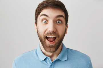 Happiest man on earth. Studio shot of excited and surprised caucasian guy smiling broadly and staring with popped eyes at camera, being thrilled to receive awesome news, posing over gray background