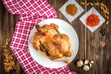 Roasted chicken on dark wooden background with spices and garlic.