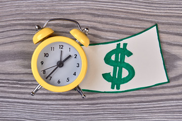 Alarm bell clock and dollar sign. Time is money concept. Wooden desk background.