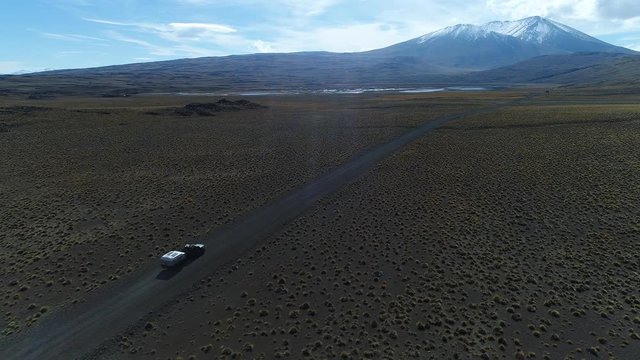 Van and trailer, motorhome in patagonia argentina riding on a gravel lonely road. Wyle mountain with snow and lagon on the background. National Park. Aerial drone scene moving right tracking car