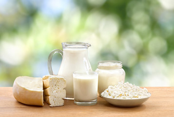 Milk, sour cream, cheese and cottage cheese on wooden table on defocused of natural background with...